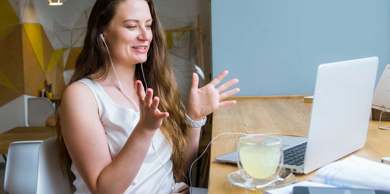 A smiling woman gestures as she talks to someone on a video call on her laptop.